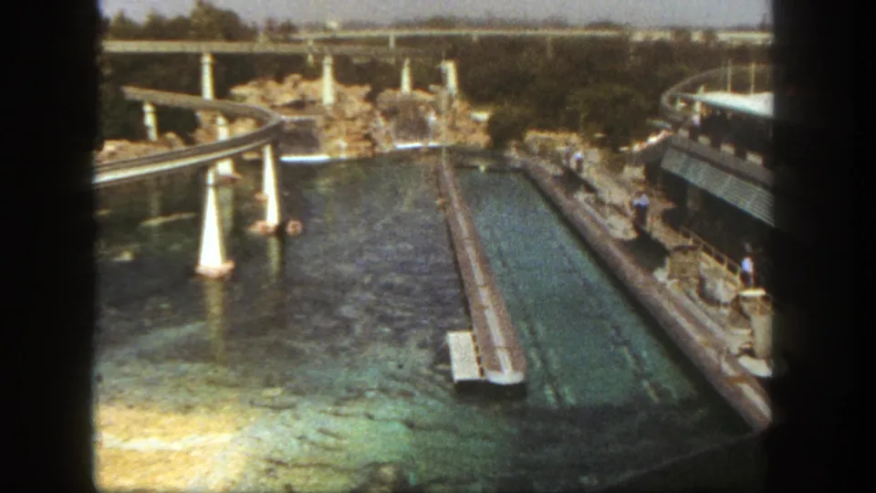 1962 Disneyland California view from above showing a long water channel, pale support columns, rockwork, walkways, and raised track.