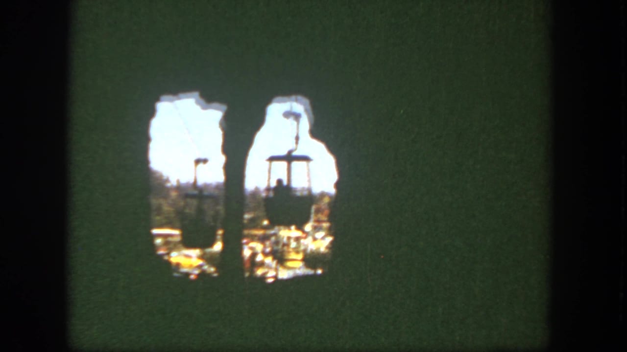 1962 Disneyland home-movie frame showing two cable cars and silhouetted riders through a rough rock-wall opening.