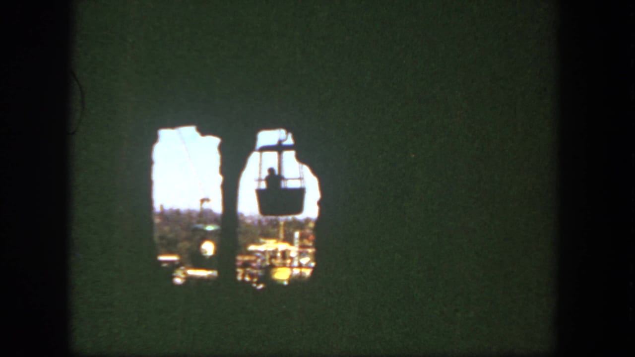 1962 Disneyland frame with suspended cable cars viewed through a shadowed rocky opening from a visitor perspective.