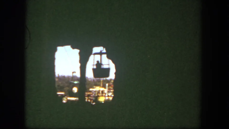 1962 Disneyland frame with suspended cable cars viewed through a shadowed rocky opening from a visitor perspective.