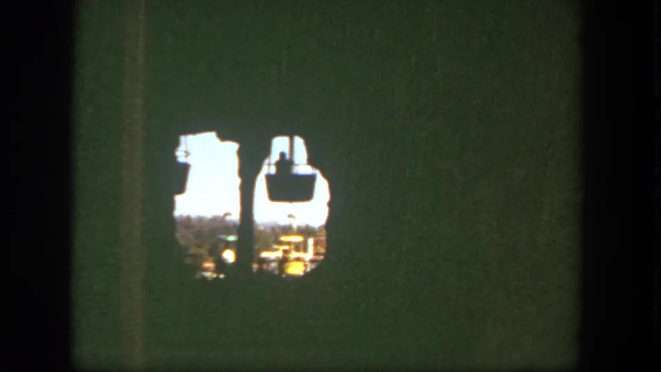 Disneyland 8mm frame from 1962 showing cable cars passing outside a rough opening with aged green film color.