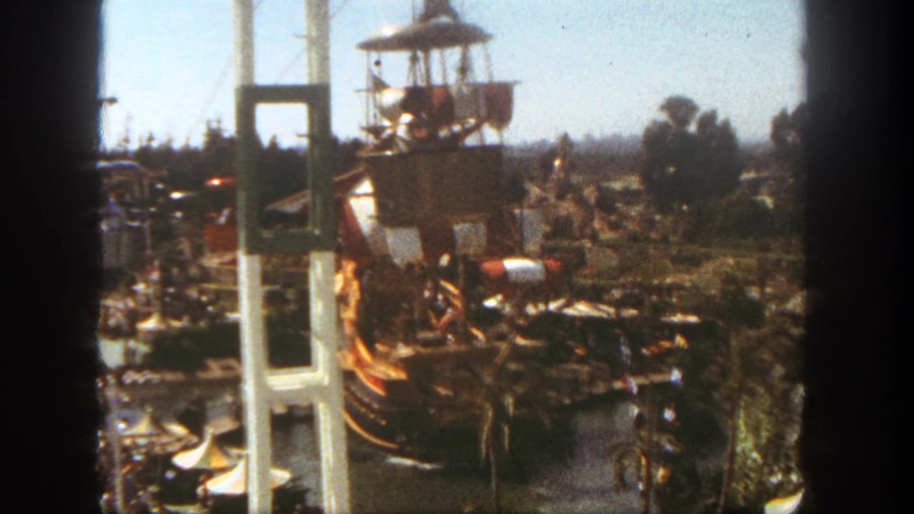 Visitor-shot 1962 Disneyland view of the pirate ship ride, support towers, nearby trees, and small figures of guests in the foreground.