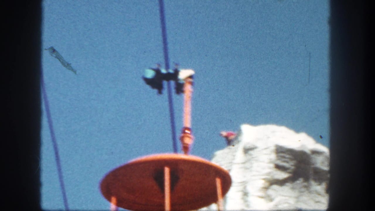 Orange Skyride bucket and cable above a pale rock formation against blue sky.