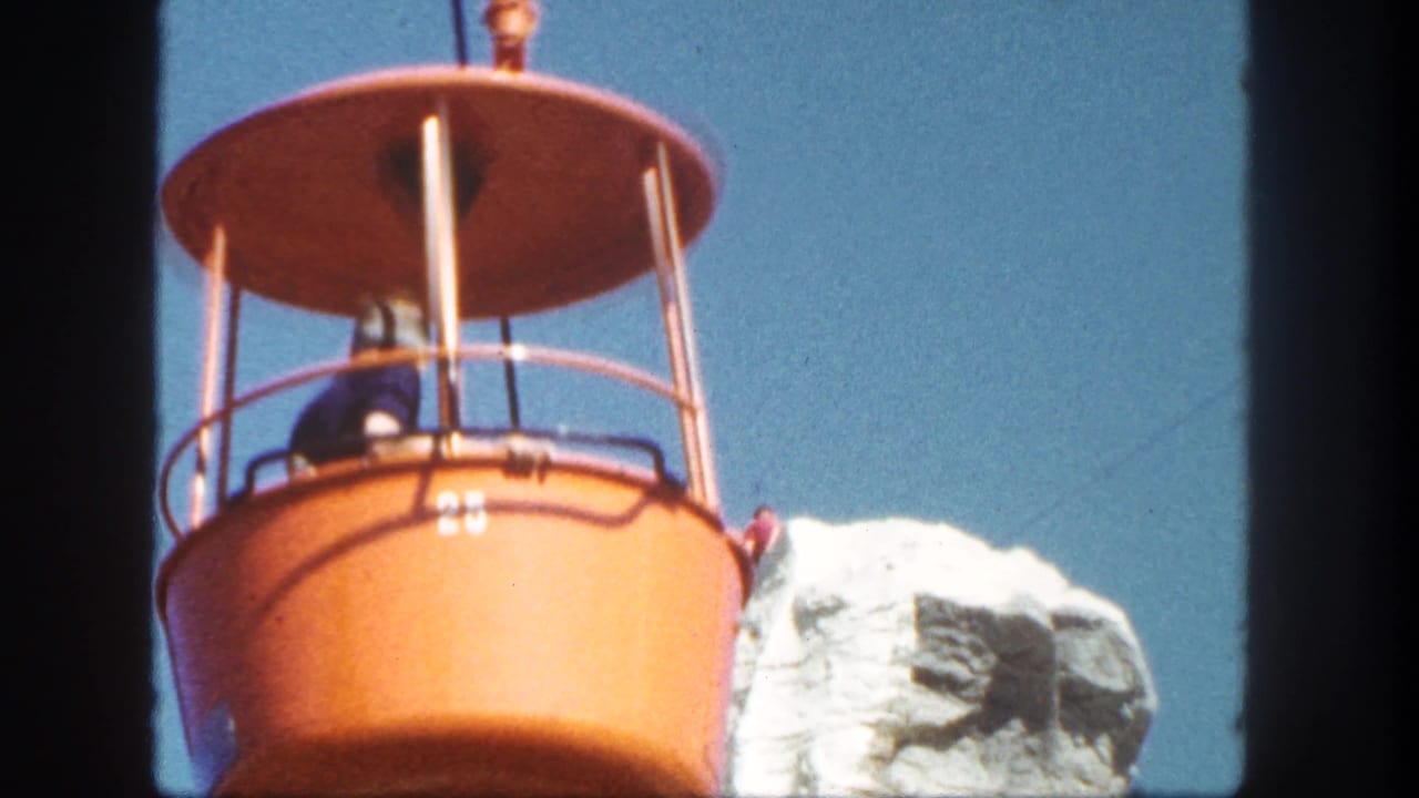 Orange gondola bucket with passengers near a white rock peak and blue sky.