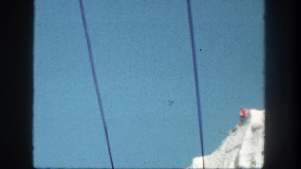 Late frame from the 1962 Disneyland clip showing Skyride cables over blue sky, with the rock formation partly visible at the lower right.