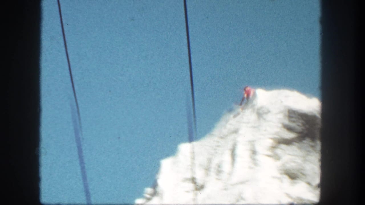 Snow-covered mountain peak under blue sky with cable lines crossing the frame.
