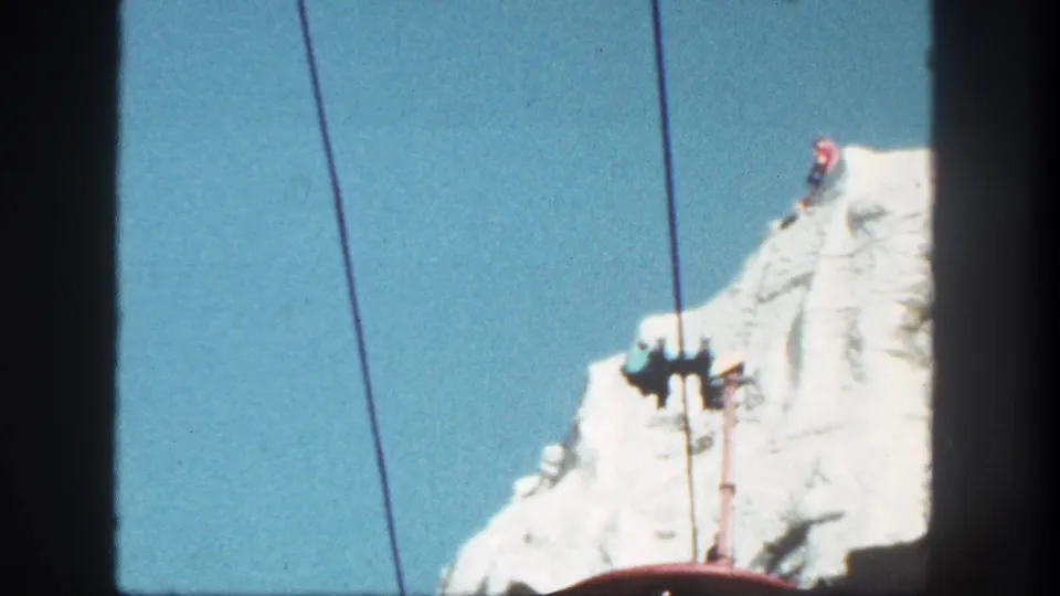1962 Disneyland 8mm frame showing cableway hardware and lines crossing a bright artificial mountain slope under clear sky.