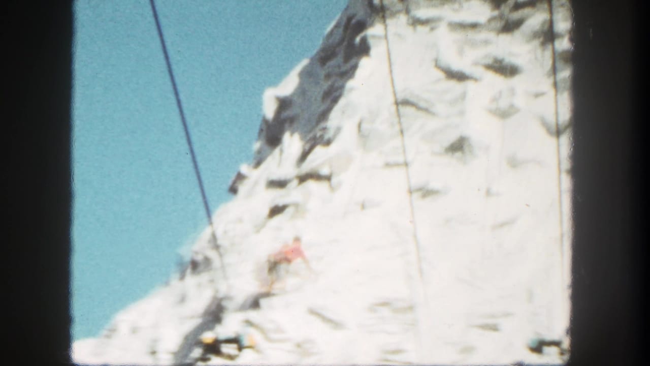 1962 Disneyland frame with snow-colored artificial rock, suspended cables, and a small red-shirted figure on the cliff.