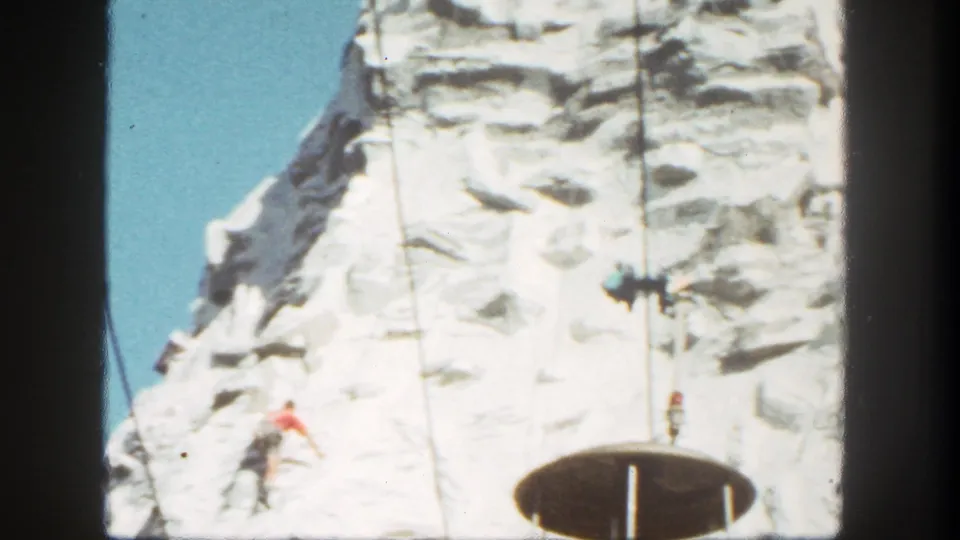 1962 Disneyland frame showing a climber on the artificial mountain, suspended cable riders, and a circular deck-like structure.