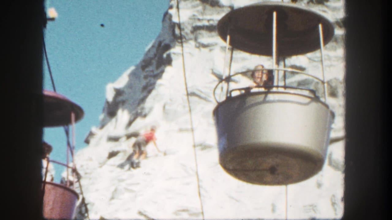 Climber on a snowy artificial mountain as a gondola bucket passes nearby.