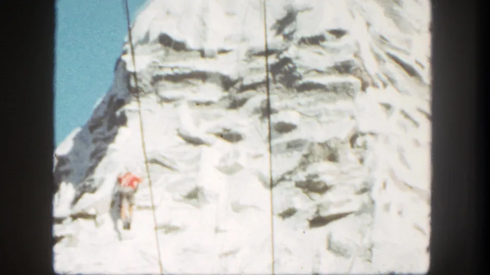 1962 Disneyland home-movie frame showing the climber on ropes against the bright artificial mountain surface.