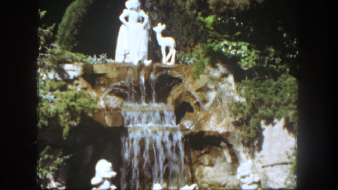 White Snow White and deer statues above a cascading rock waterfall with greenery around the display.