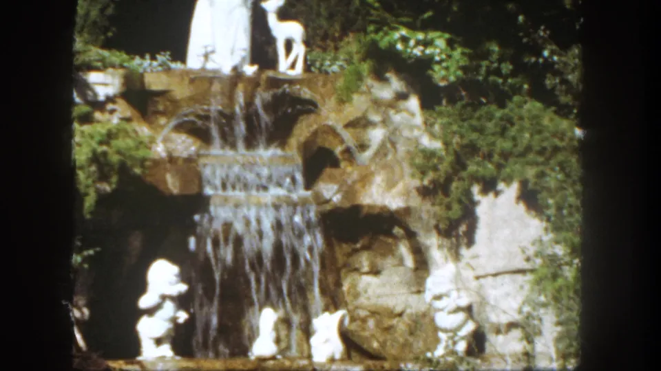 1962 Disneyland home-movie frame showing the waterfall display with white figures near the base and the Snow White and deer statues above.