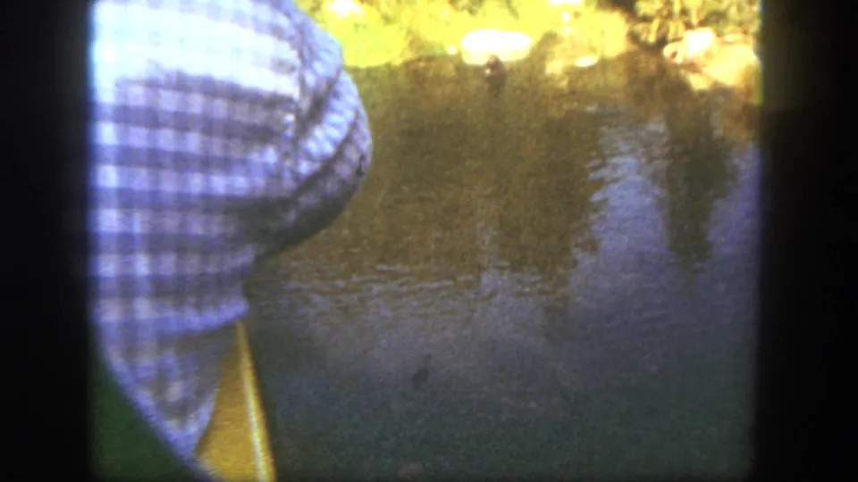 1962 Disneyland home-movie view of a cropped visitor standing near lake water with warm reflected light.