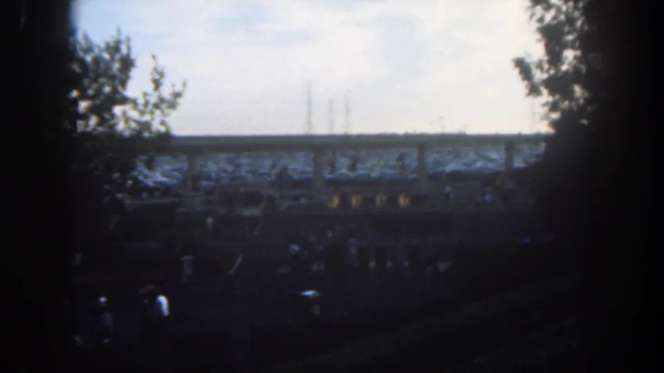 Soft 8mm frame of Disneyland visitors in 1962, with a raised structure across the background and dark vignetting at the edges.