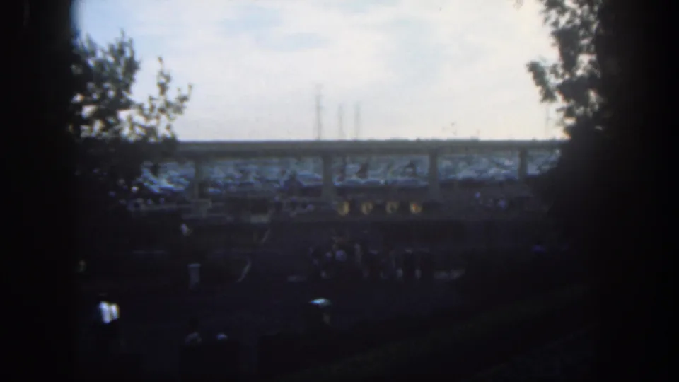 1962 Disneyland home-movie still with distant visitors, silhouetted trees, and an elevated structure crossing the frame.