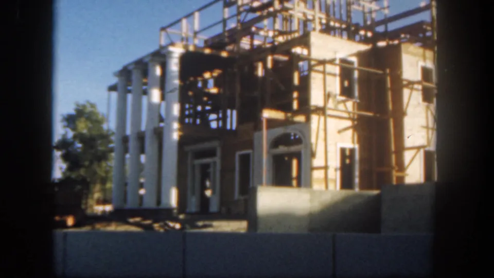 1962 Disneyland frame showing the columned construction facade behind barriers, with trees at the side and dark scan edges.
