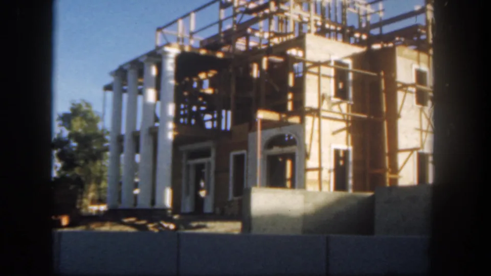 1962 Disneyland view of a columned building under construction, with timber scaffolding and barriers in the foreground.