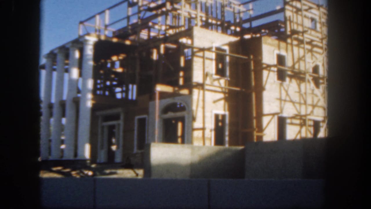 A visitor-shot 1962 Disneyland frame showing a sunlit facade under construction, with columns, brickwork, and scaffolding.