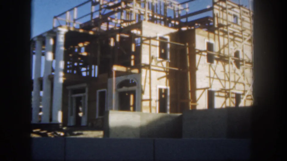 Closer 1962 Disneyland construction view with white columns, dark window openings, timber scaffolding, and temporary barriers.