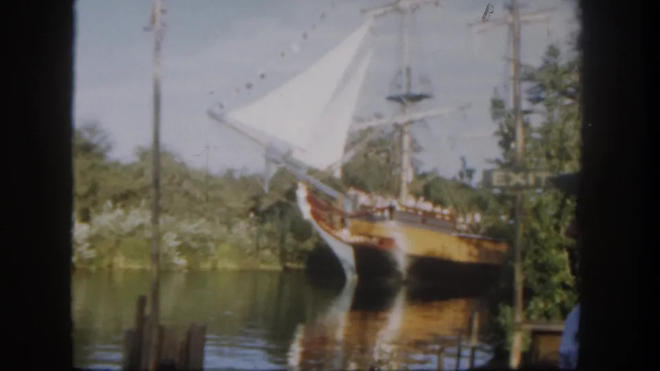 1962 Disneyland waterfront view of a white-sailed clipper-style ship near trees, water, and a visible EXIT sign.