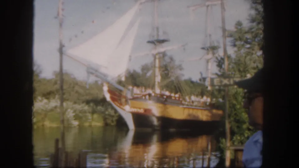 1962 Disneyland California footage frame showing the ship attraction closer in view, with sails, rigging, water reflections, and a partial visitor.