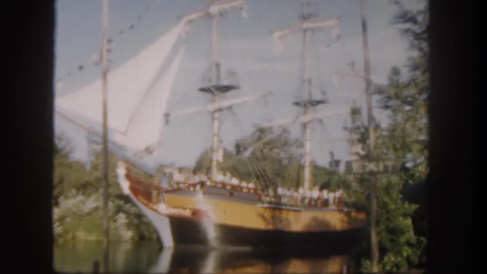 Soft 1962 Disneyland home-movie frame showing the sailing ship attraction, rigging, visitors, trees, and water in a slightly shifted view.