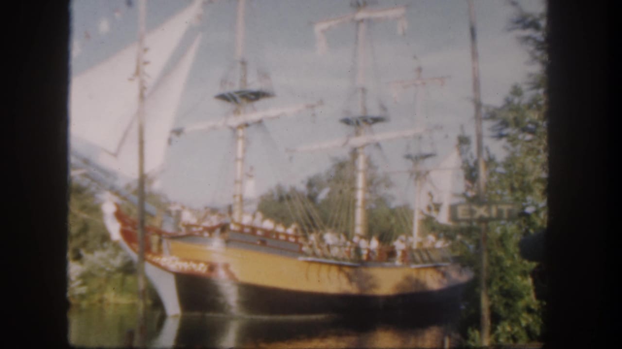 Sailing ship with passengers passes an EXIT sign beside trees.