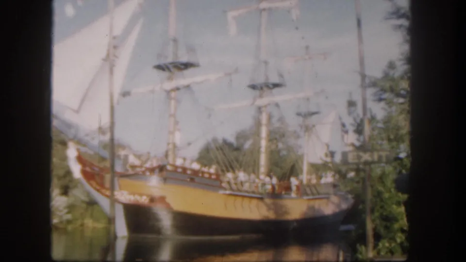 Soft 8mm frame from Disneyland in 1962 showing the ship's painted hull, tall masts, pale sails, rigging, and passengers on deck.