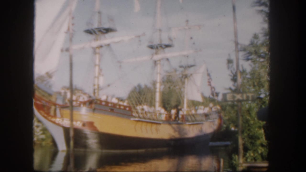 1962 Disneyland home-movie frame showing a yellow and red replica sailing ship carrying guests through a waterway.