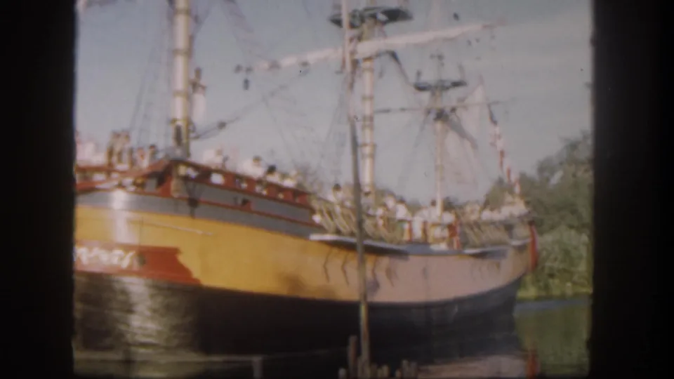 1962 Disneyland frame with the replica sailing ship passing near a foreground pole, guests visible on deck.