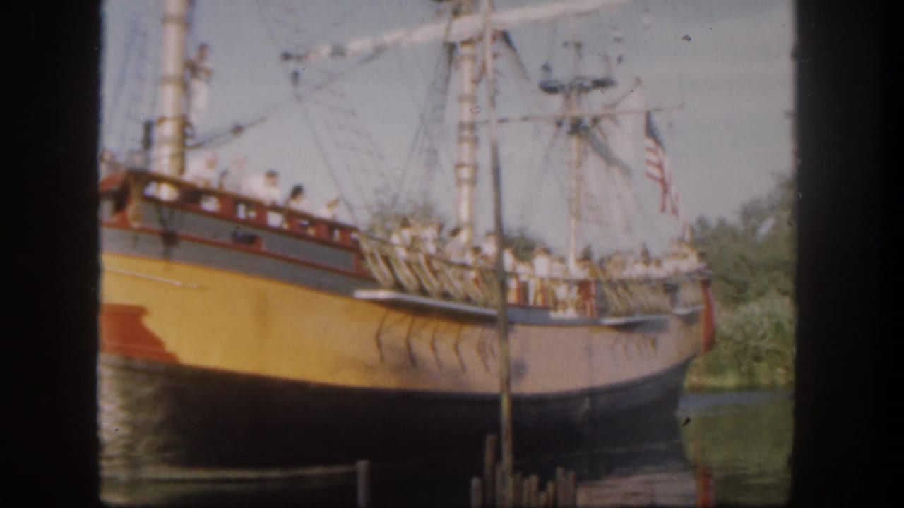 Yellow-hulled replica sailing ship docked beside water with rigging and an American flag.