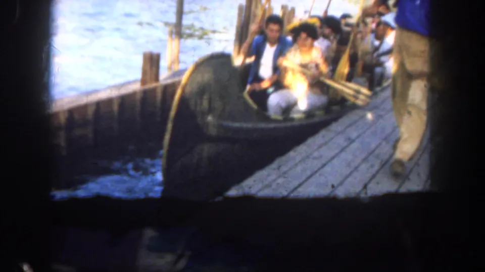 1962 Disneyland waterfront frame showing visitors in a small dark boat beside dock posts, rope, and sunlit water.