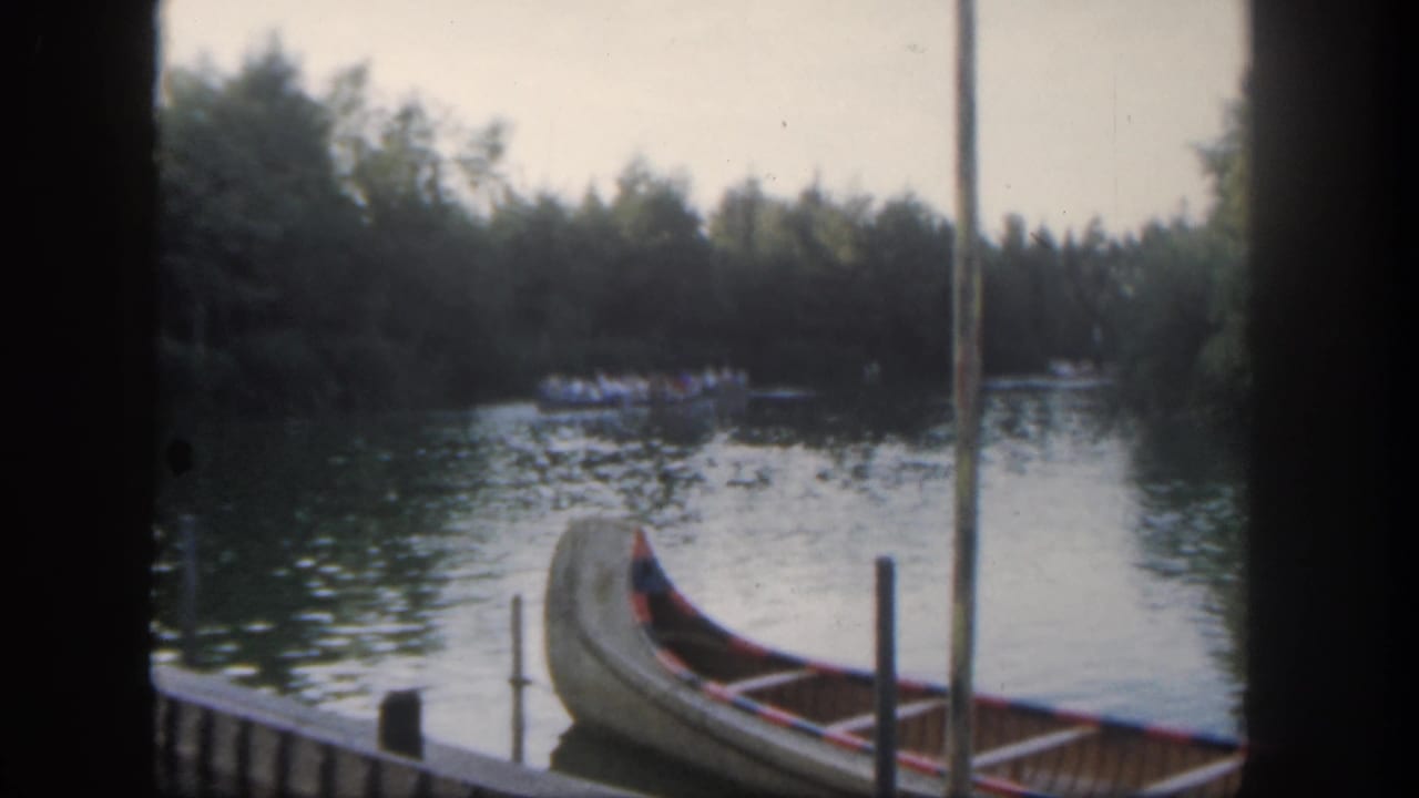 1962 Disneyland river view with a docked canoe in the foreground and a small guest boat visible near the far bank.