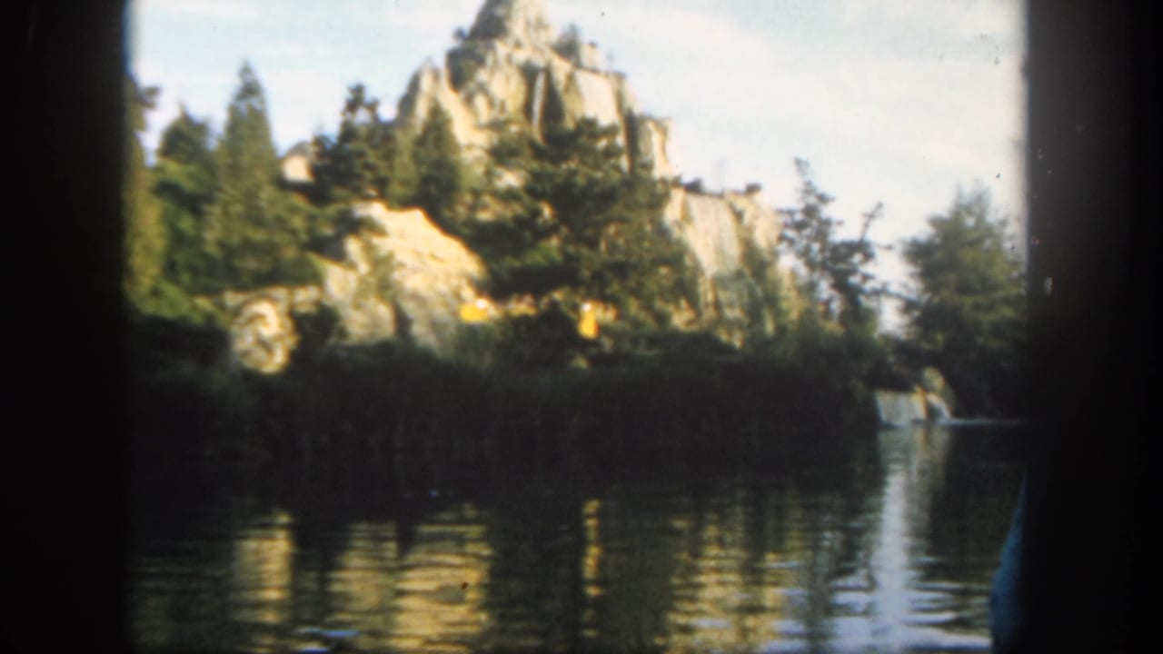 Rocky shoreline and trees reflected in dark water, with a canoe at right.