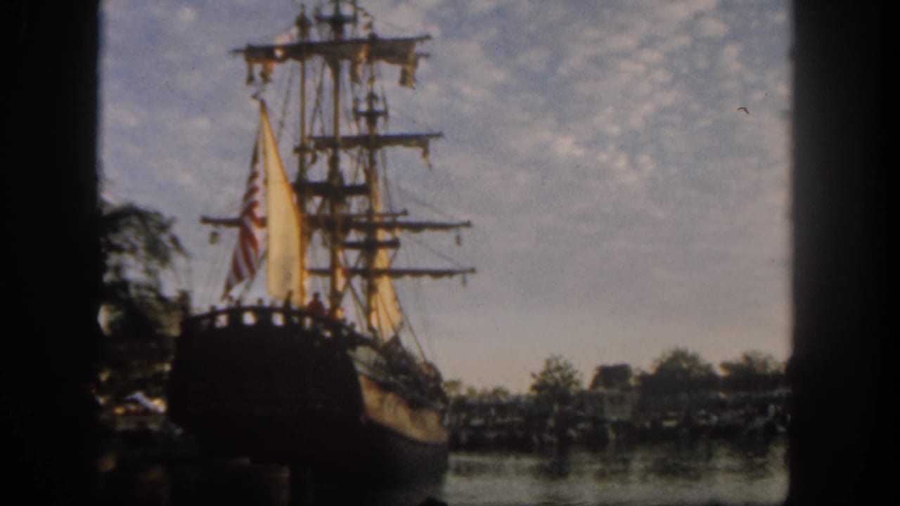 Visitor-shot 1962 Disneyland view of a moored sailing ship, its masts and American flag visible against a partly cloudy sky.