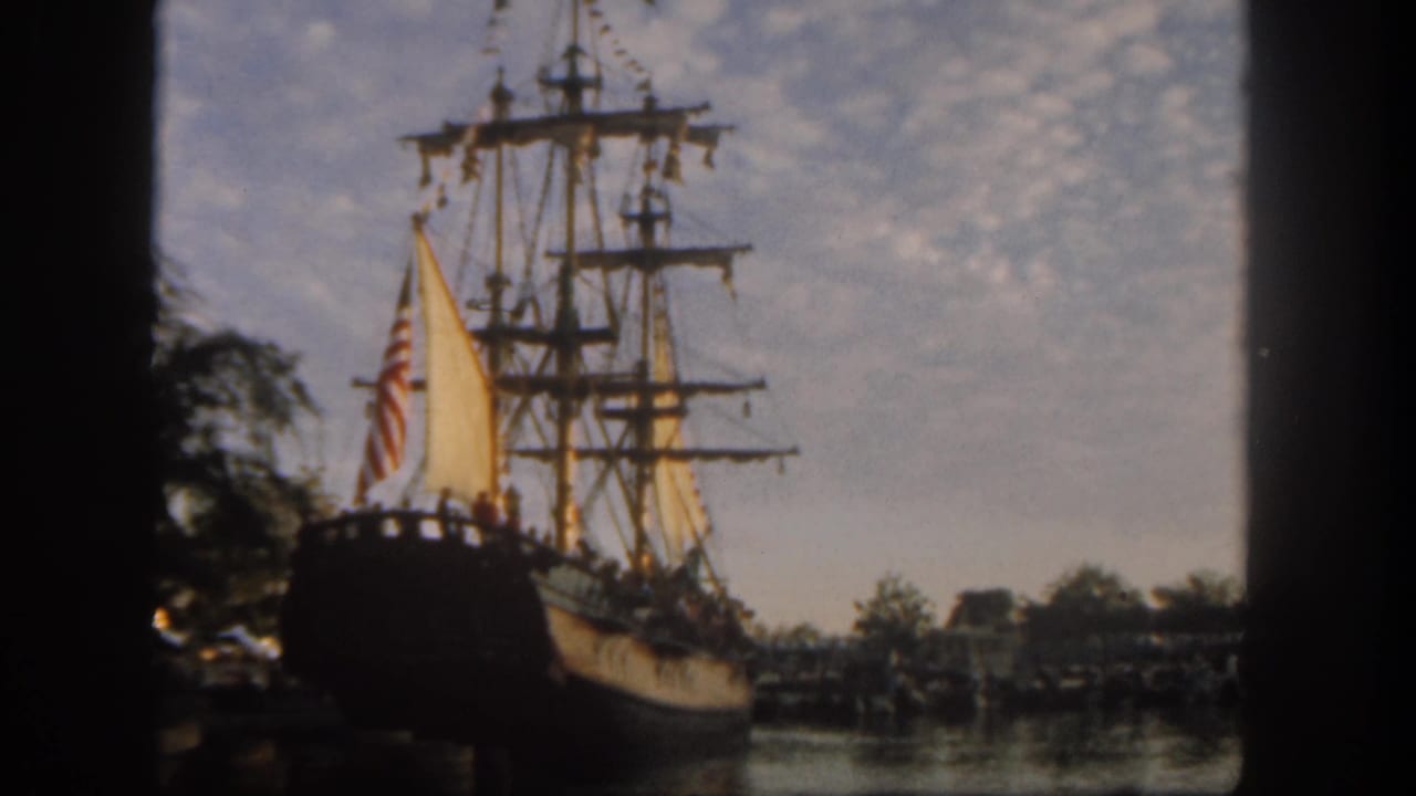 Tall wooden sailing ship with yellow sails and American flag on a park waterfront.