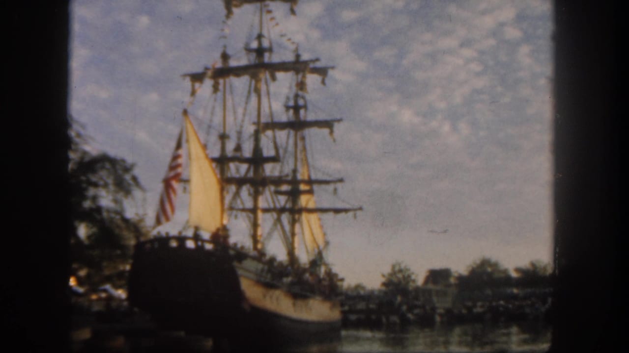 Wooden sailing ship with yellow sails viewed through a dark frame by the water.