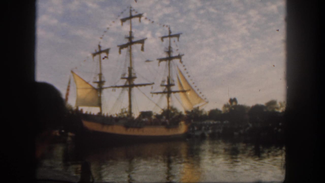 Multi-masted sailing ship on water seen through a dark foreground frame.