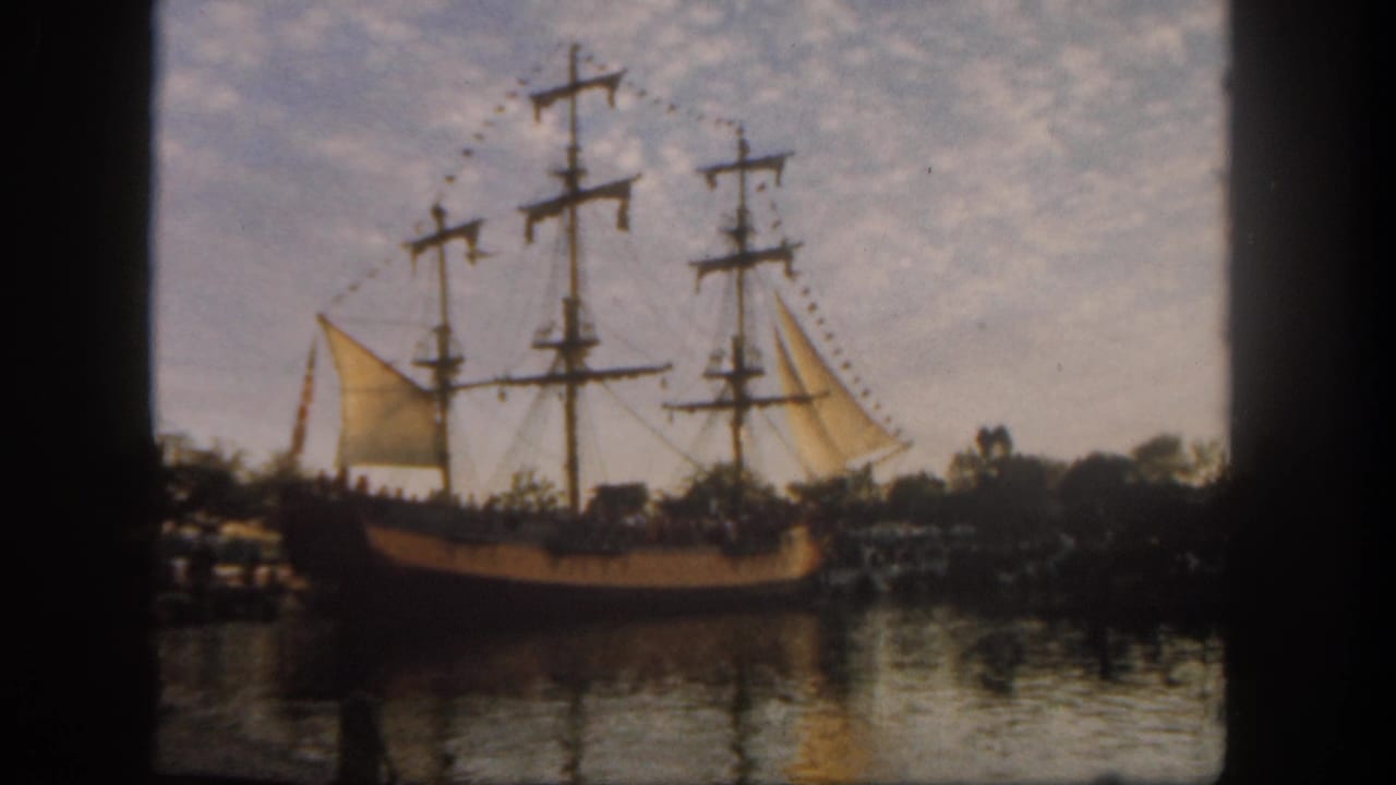 Visitor-shot 1962 Disneyland view of a multi-masted sailing ship with sails and pennants on calm water.