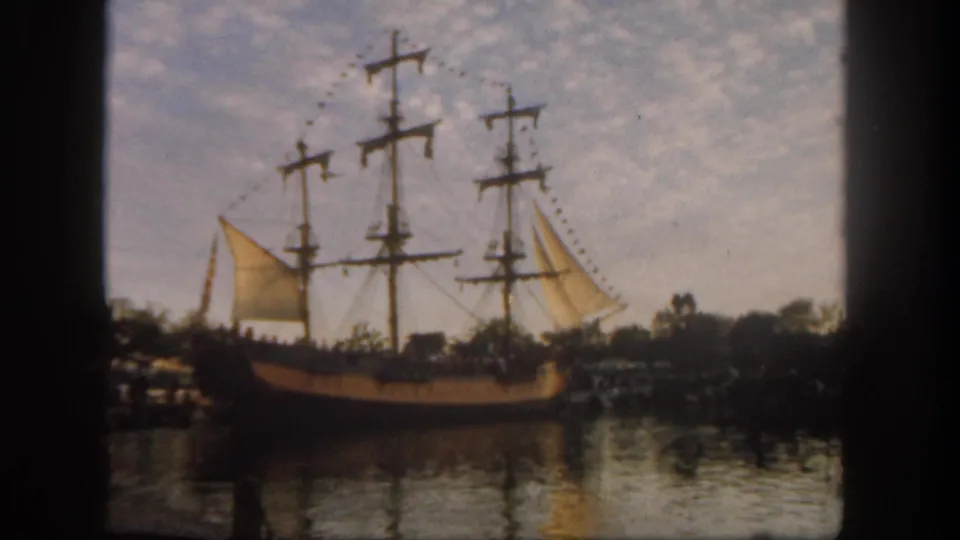 Visitor-shot 1962 Disneyland view of a multi-masted sailing ship with sails and pennants on calm water.