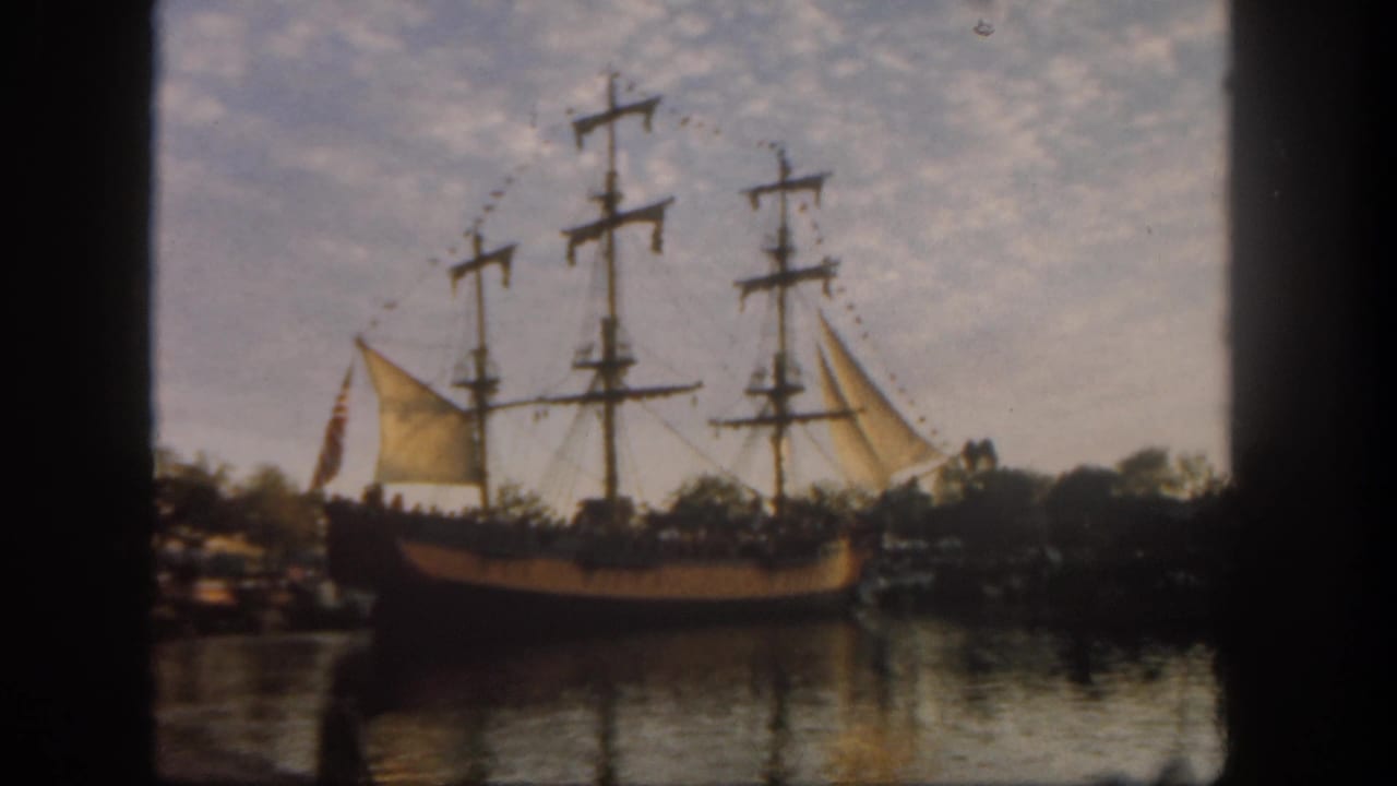 1962 Disneyland home-movie frame showing a pirate-style ship beside water, with masts, raised sails, reflections, and 8mm film edges.