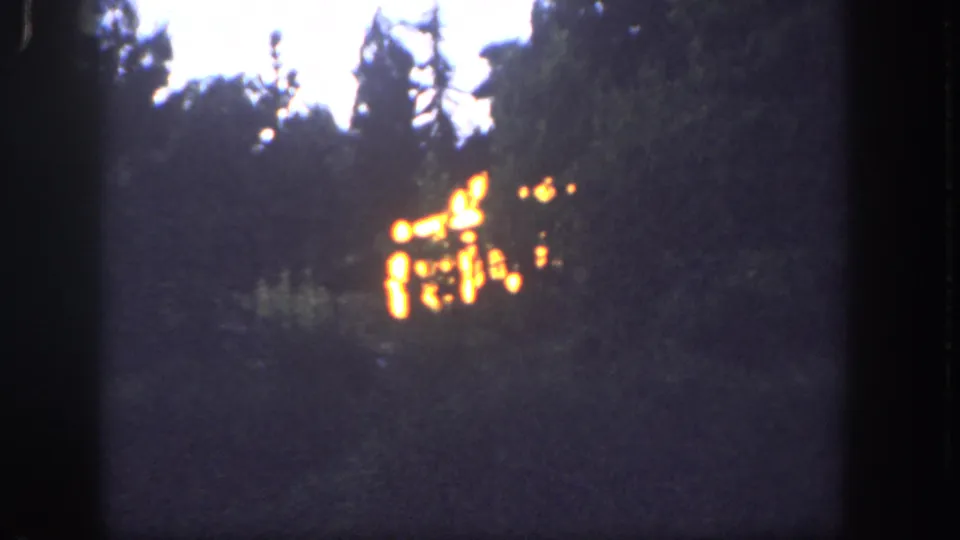 1962 Disneyland home-movie frame with bright firelight in a dark wooded area, surrounded by grain, soft focus, and film-edge framing.