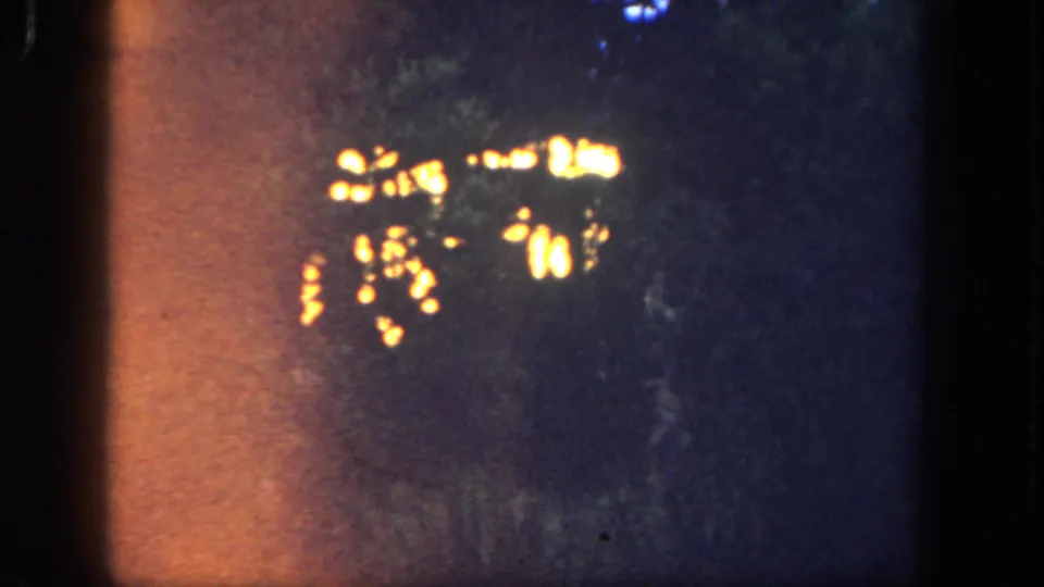 1962 Disneyland 8mm night view with clustered warm lights and a broad orange film flare at the left edge.