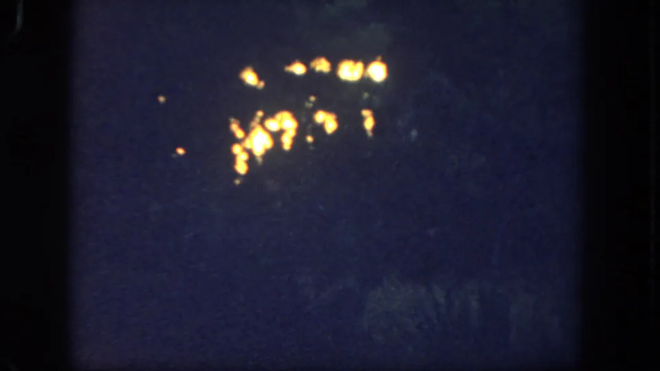 1962 Disneyland 8mm frame showing small warm light clusters against a dark blue-black night scene.