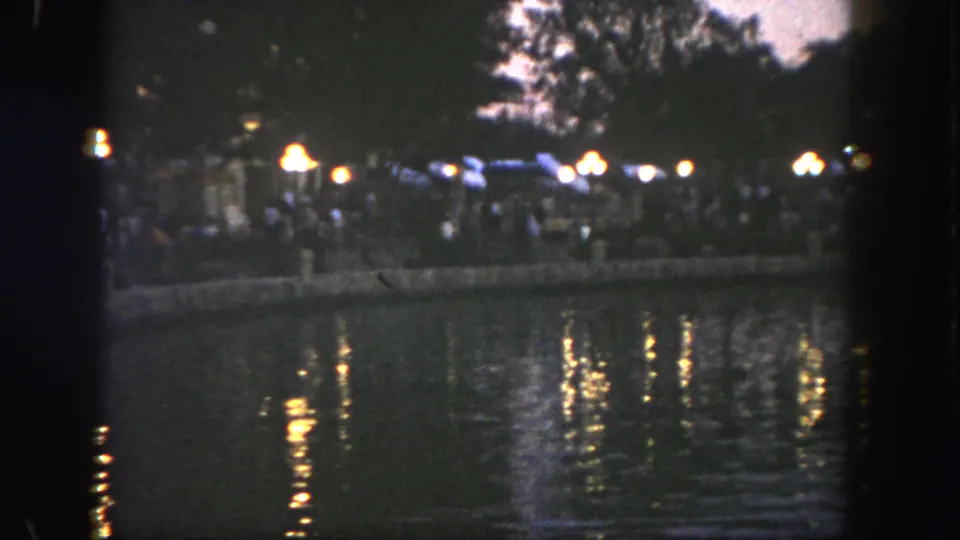 1962 Disneyland home-movie frame showing distant shoreline lights reflected across a dark lake at night.