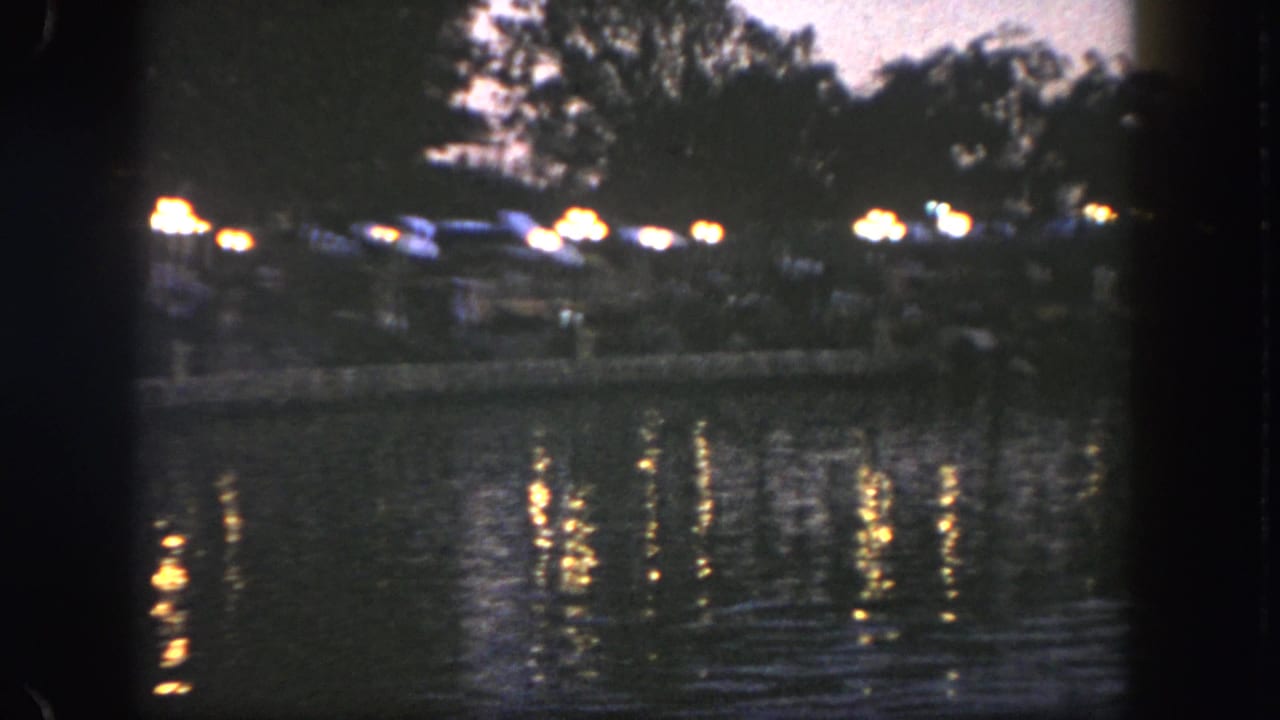 Night view across water at Disneyland, with soft 8mm exposure and small groups along the far shore.