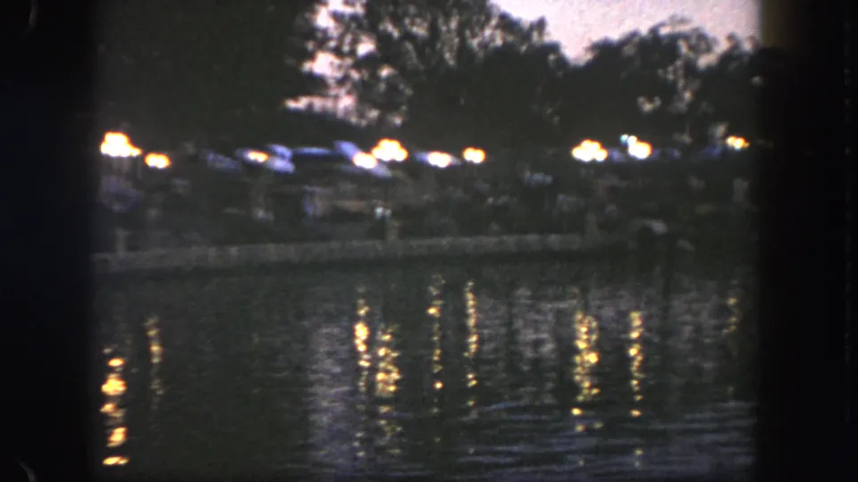 Night view across water at Disneyland, with soft 8mm exposure and small groups along the far shore.