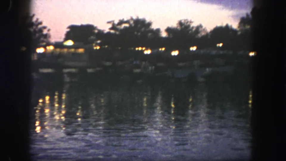 1962 Disneyland lake scene with warm point lights, dark trees, and a visitor-shot nighttime composition.