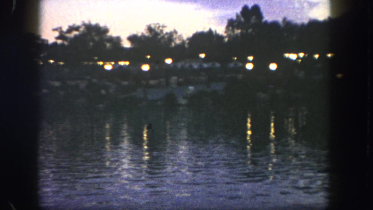 1962 Disneyland waterfront view at twilight, with small lights along the far shore and reflections stretching across the bay.